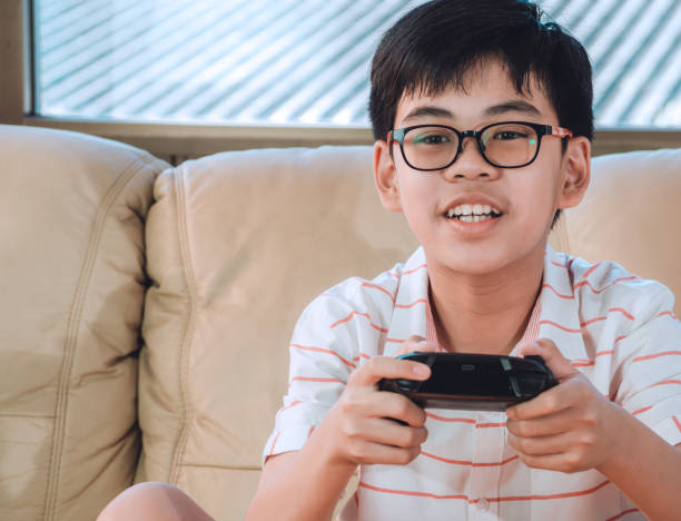 istock Excited asian boy are playing game console, controller or videogame joystick console looking at TV screen in hand on sofa at home. 1301422328