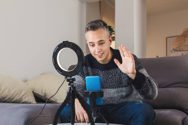 istock Young man millennial influencer sit on couch is vlogging, recording and creating online content with smartphone and lights. Social media video channel recording concept 1301423696