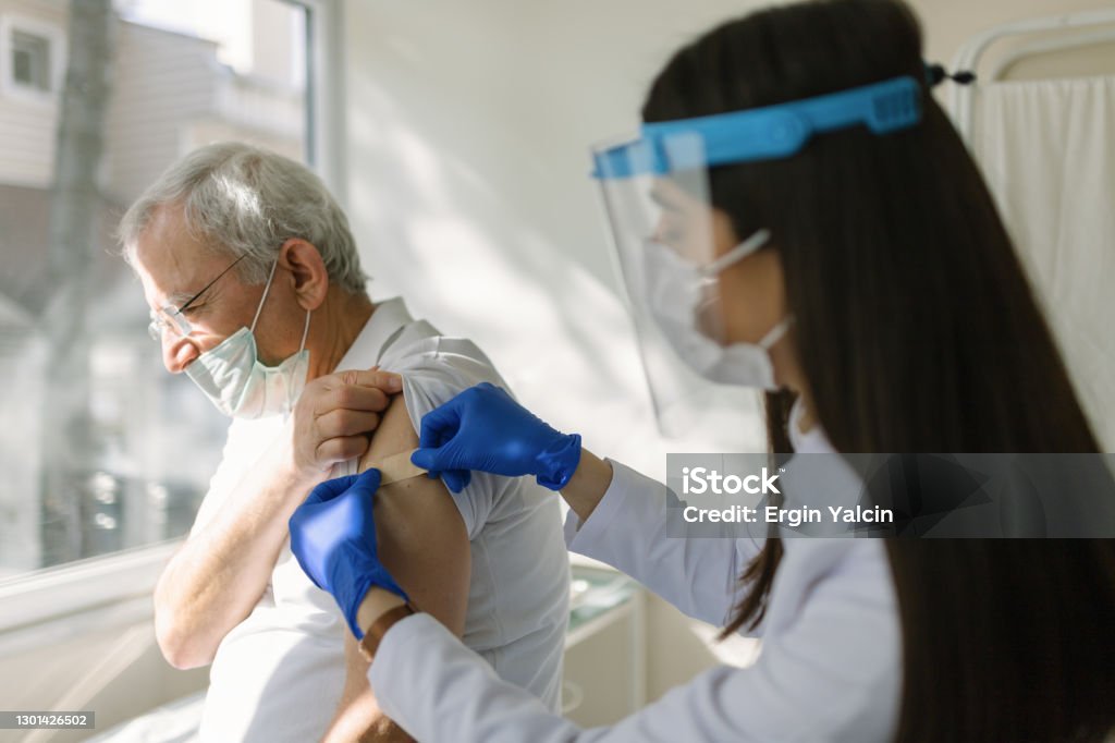 Female doctor wearing protective suit injecting vaccine into senior patient's arm Vaccination Stock Photo