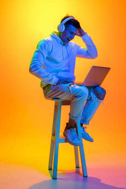 Caucasian beautiful man's portrait isolated on yellow studio background in multicolored neon light