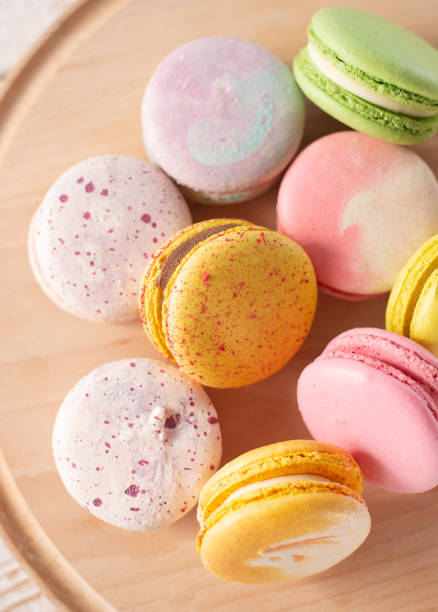 istock Multi-colored macarons on wood background with soft lights and shadows. Gentle macaroons on table on light background 1301429070