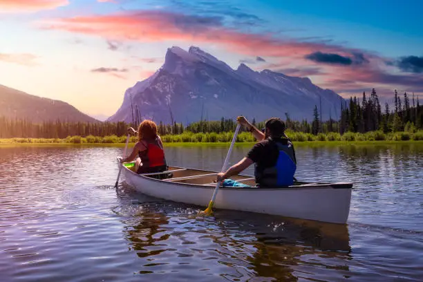 Photo of Couple adventurous friends are canoeing in a lake surrounded by the Canadian Mountains.