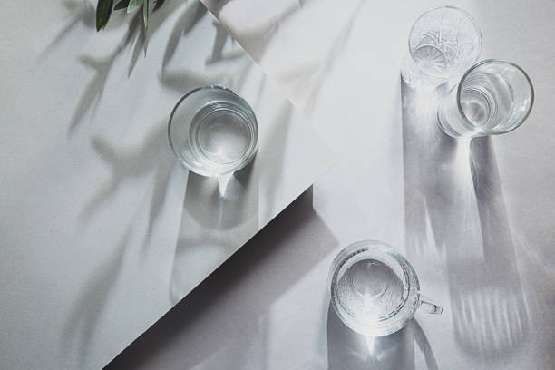 istock Glasses of water top view summer composition on light background. Still life with olive branch and long shadows, with copy space 1301433507