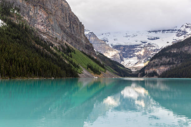 Lake Louise in the Morning, Alberta, Canada. The water is turquoise colored and the sky is cloudy. It is an overcast summer day.