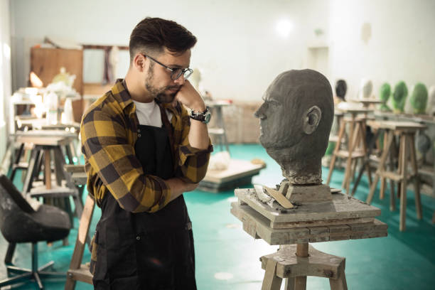 istock Young Male Sculptor working on a clay bust ,looking at it and thinking 1301435690