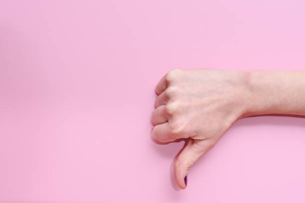 mano de una mujer caucásica haciendo gesto de pulgares hacia abajo sobre un fondo rosa - pessimist women one person caucasian fotografías e imágenes de stock