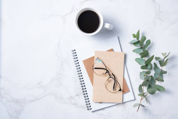 istock Flat lay with  eucalyptus flower, cup of coffee,  a glasses, a craft notebook  on a marble table. Women's floral desktop. morning concept 1301438279