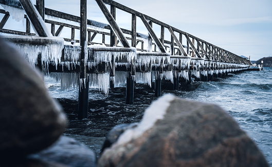 Frozen jetty at the ocean with huge icicles hanging at the wooden planks