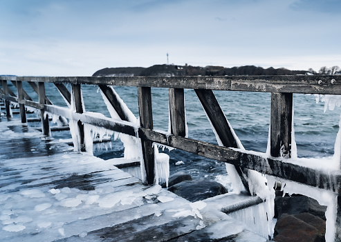Frozen jetty at the ocean with huge icicles hanging at the wooden planks