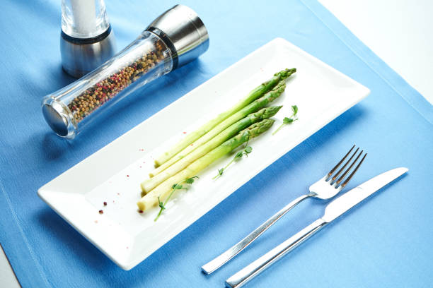 Delicious side dish for main courses - boiled asparagus with microgreen in a white plate on a blue tablecloth