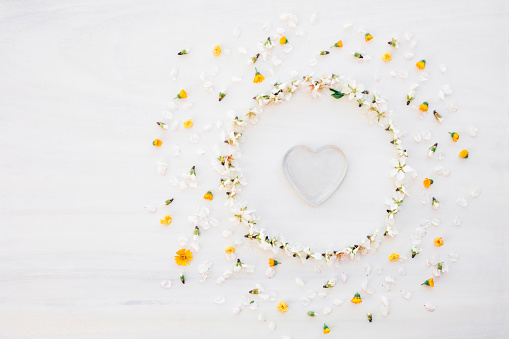 Beautiful flat lay of a beautiful mandala with almond blossoms, white petals, yellow meadow flowers with a transparent glass heart in the centre and copy space on the left side. Slightly grain added. Part of a series.