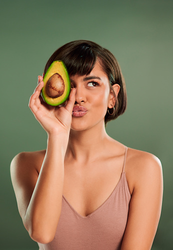 Shot of a beautiful young woman holding up a halved avocado against her face