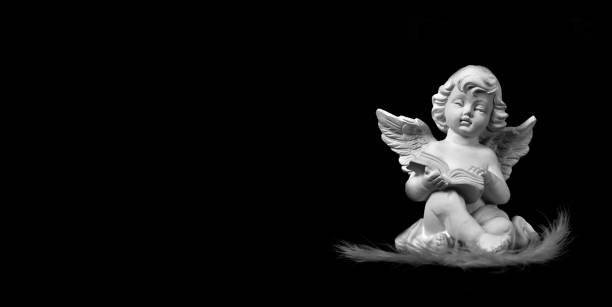 istock Angel sitting and reading book isolated on black background 1301442505