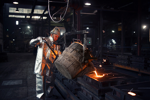 Fundición de hierro en fábrica de fundición. Trabajador de fundición vertiendo acero líquido en moldes. photo