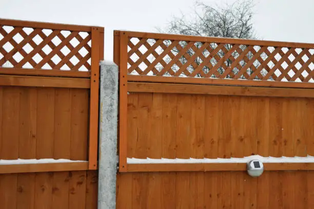 New orange painted traditional wooden panel fence with criss cross lattice trellis privacy screening on top. Property boundary. Outdoors on a cold freezing winters day with snow and ice on the fence.  Billericay, Essex, United Kingdom, February 8, 2021.