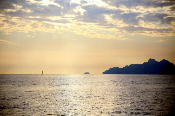 istock Sunset light on an isolated sailboat, sailing on the horizon, with the coast in backlight, under a dramatic sky 1301445164