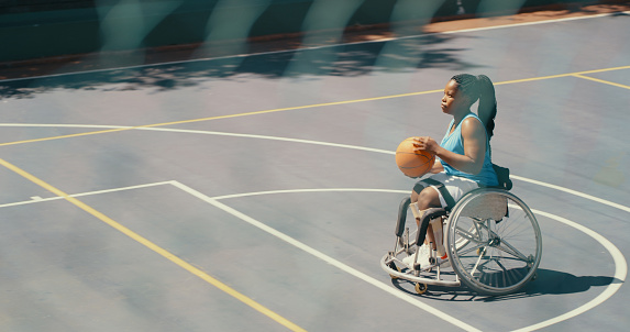 Shot from the outside of an outdoor court of a young female wheelchair basketball player taking a free throw