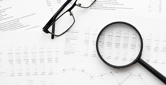 Spectacles and magnifying glass on financial statement and balance sheeet on desk of auditor. Business and financial research concept.