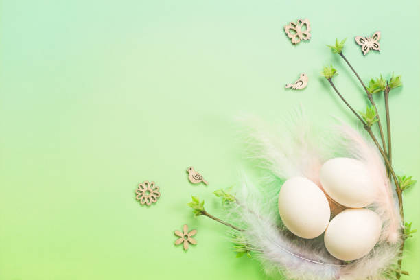 istock White Easter eggs in a delicate nest of colored feathers with unfurled leaf buds on the branches. Spring, a religious holiday, the birth of life. Copy space. Pale green background 1301447980