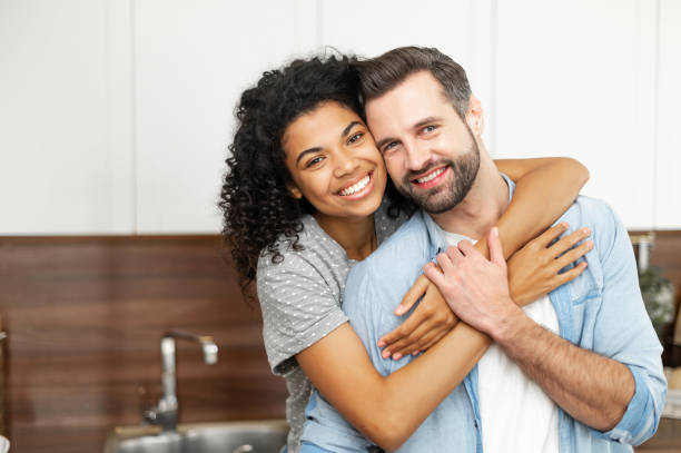 pareja interracial abrazándose en la cocina - couple young adult african descent multi ethnic group fotografías e imágenes de stock