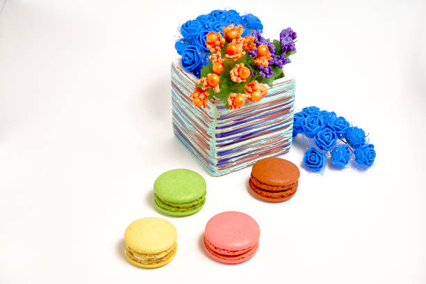 Composition with sweet tasty macaroons and vase with flowers on white background.