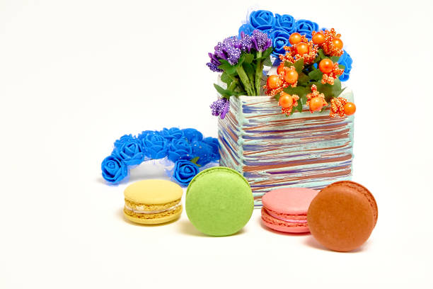 Composition with sweet tasty macaroons and vase with flowers on white background.