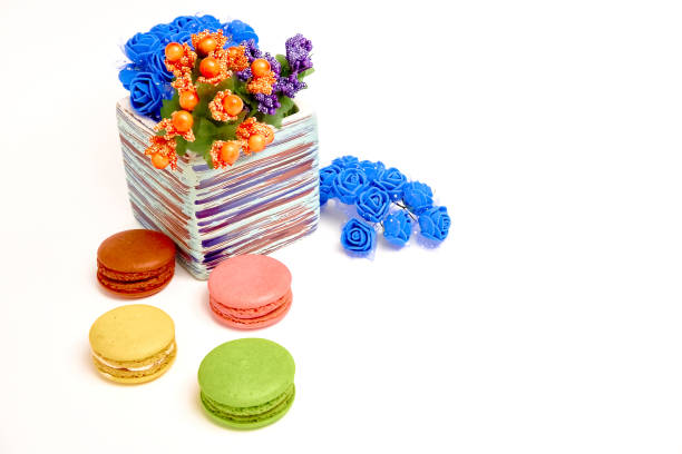 Composition with sweet tasty macaroons and vase with flowers on white background.