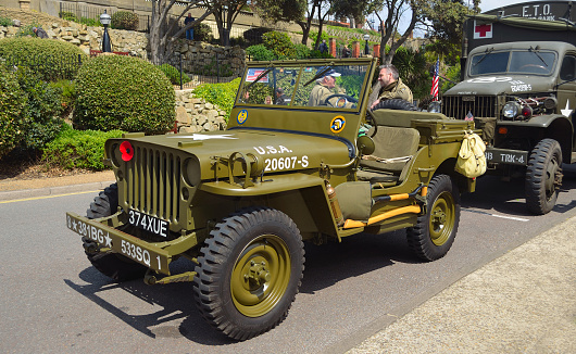 Felixstowe, Suffolk, England -  May 07, 2017: Classic WW2 Jeep  parked on street with men in uniform in background.