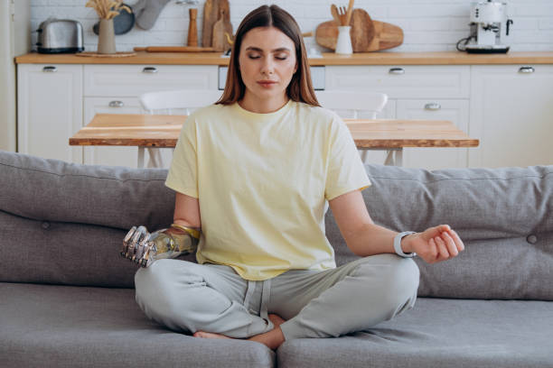 istock Woman with a bionic prosthetic arm sits at home on a sofa in a lotus position and meditates 1301458876