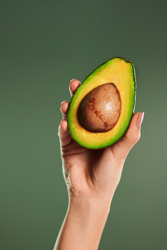 Cropped shot of a woman holding up a halved avocado against a green background