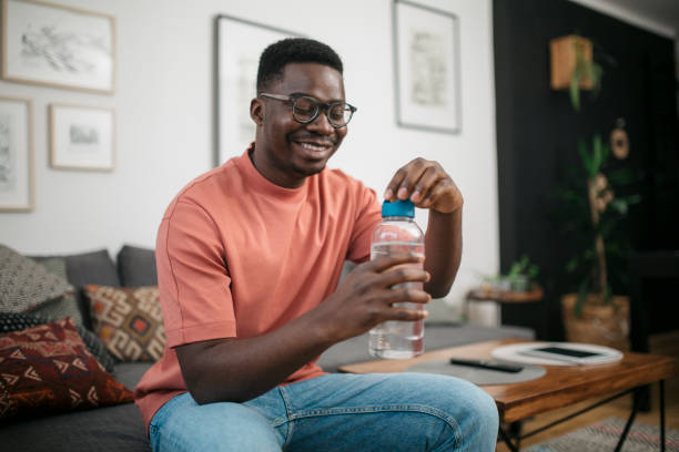istock Happy young African American man drinking water at home 1301464191