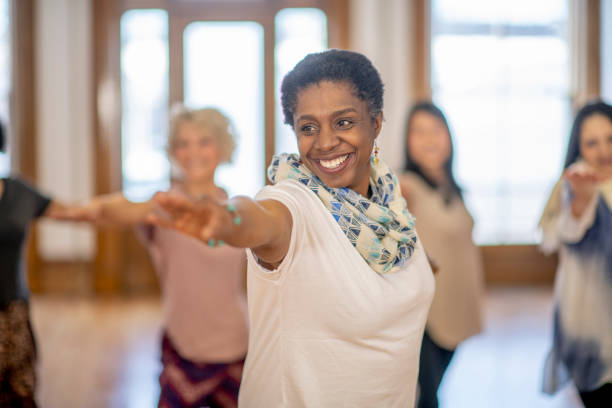 Senior adult participating in yoga class A senior female adult of African descent is participating in a group yoga class. The group is doing the Warrior Pose in class. She is happy and smiling. exercise class stock pictures, royalty-free photos & images