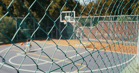 Shot from the outside of an outdoor court of a wheelchair basketball player practicing drippling alone