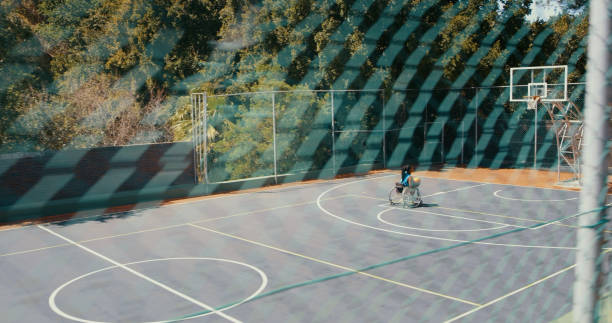 Shot from the outside of an outdoor court of a wheelchair basketball player practicing alone
