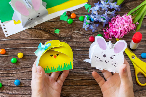 istock Child holds a box for packing sweets with Easter bunny and Easter chick. Handmade. Project of children's creativity, handicrafts, crafts for kids. 1301469838