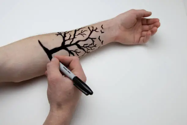 Drawing a tree with a black permanent marker on forearm
