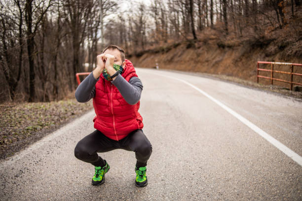 istock The athlete does exercises before training, warms up the muscles. Athlete doing exercises on the road in nature. An athlete who runs outdoors for exercise and fitness - Athletic Man 1301477921