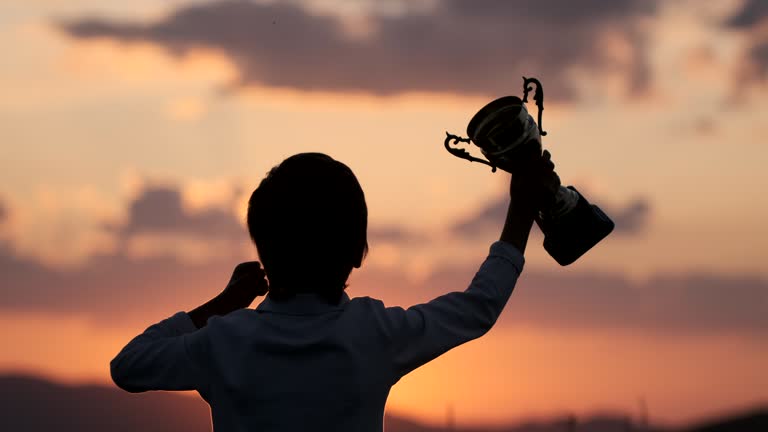 Silhouette of happy champion little boy child holding up golden trophy cup in hand