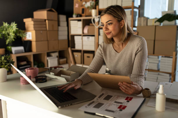 istock Smiling young businesswoman using laptop and reviewing data from a clipboard 1301482046