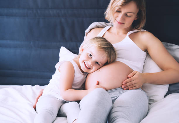 madre e hija embarazadas descansando en la cama en casa. joven con su primer hijo durante el segundo embarazo. concepto de maternidad y crianza. niña pequeña y mamá. - offspring child lying on back parent fotografías e imágenes de stock