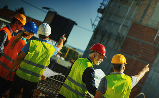 Closeup rear view of construction engineers and contractors having a meeting at a construction site. They are looking at the building and discussing the development process.