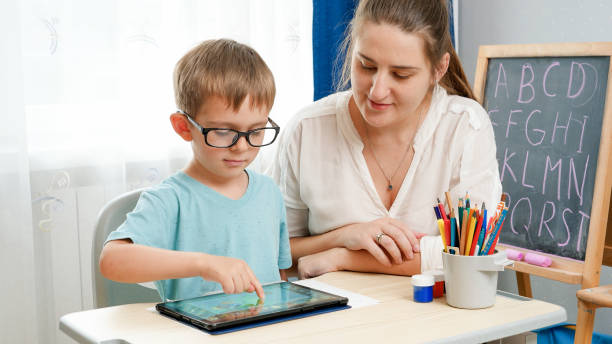 istock Little boy in eyeglasses playing on tablet computer. Mother hugging her little son doing homework using gadet. Children having problems with eyes and sight 1301487669