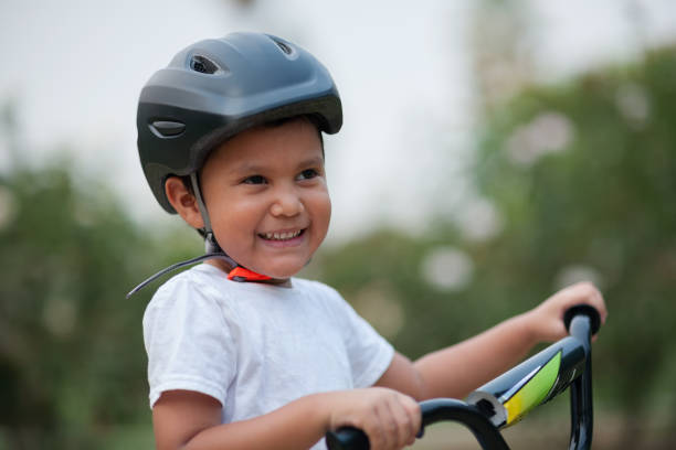 A four year old boy smiles, while wearing his bicycle helmet for safety and holding on to the bike's handle bars. stock photo