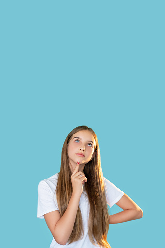 Curious teen girl. Commercial background. Special offer. Portrait of doubtful thoughtful young lady in white t-shirt thinking looking up at copy space isolated on blue.