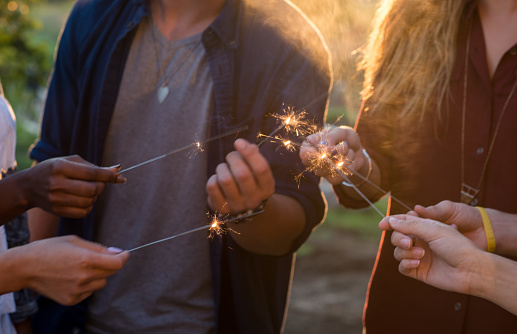 A group of young adults holding lit up some sparklers during their party outdoors.