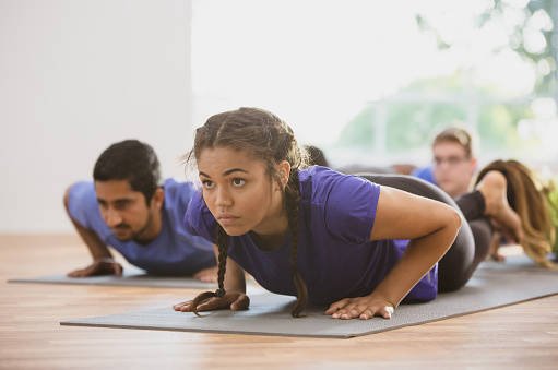 An athletic female adult is participating in a group yoga class. The class is doing a low cobra pose.