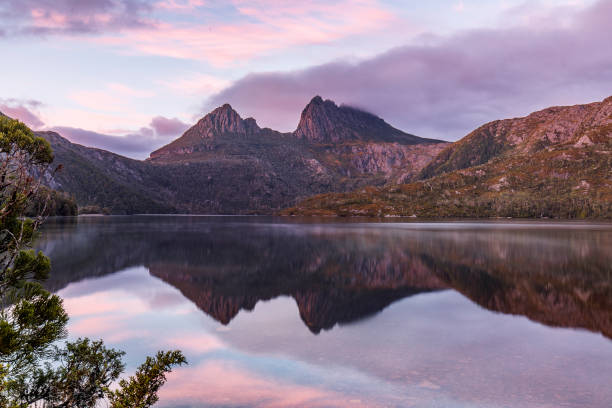 istock Colourful mountain range reflected in still lake with pink sky 1301497870