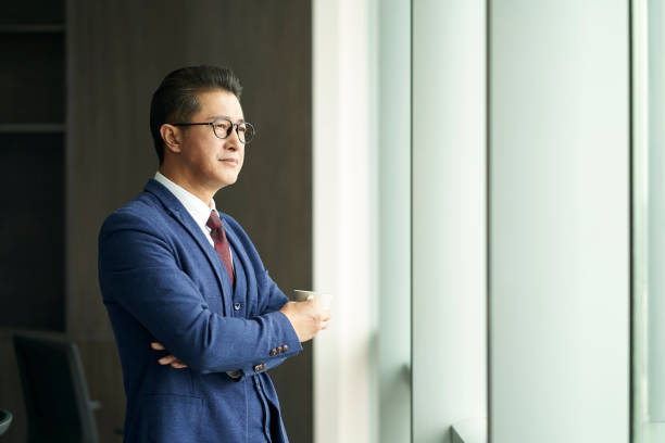 asian business manager standing in front of window thinking - business business person ceo coffee imagens e fotografias de stock