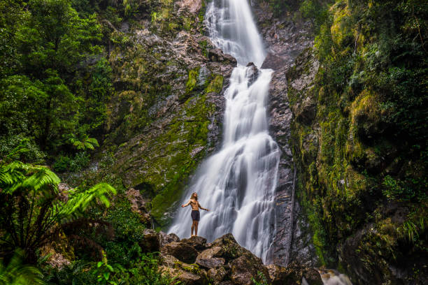 istock Young man standing below waterfall, with green moss and dense rainforest environment 1301506781