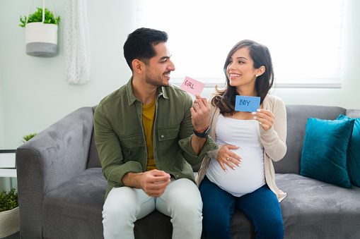 Excited and happy pregnant couple doing a gender reveal of their new baby. Handsome man and beautiful woman looking at each other while holding a pink a blue sign with girl or boy